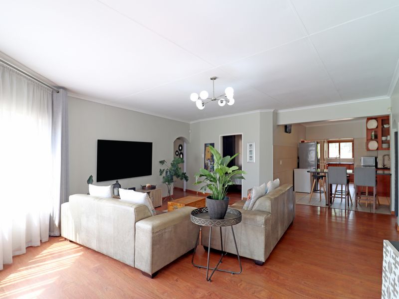 Open plan living area featuring laminate flooring and a connected kitchen space with built-in cabinetry and breakfast bar seating.