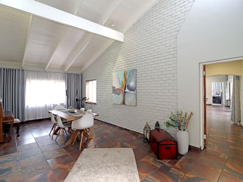 Spacious dining area featuring a high vaulted ceiling with exposed beams, a textured painted brick feature wall, and durable tiled flooring.