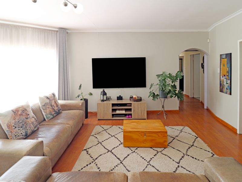 A well-maintained living room featuring warm-toned laminate flooring, a classic archway leading to the hallway, and clean, neutral wall finishes.