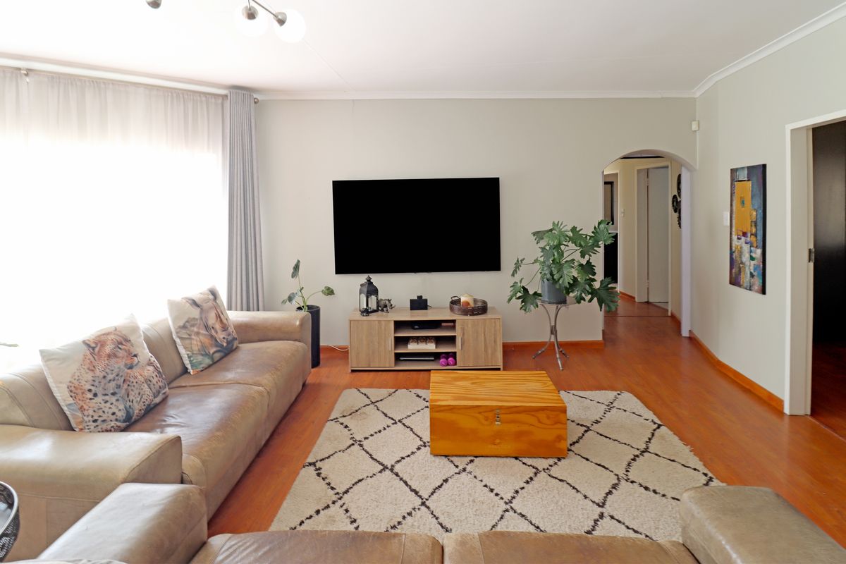 A well-maintained living room featuring warm-toned laminate flooring, a classic archway leading to the hallway, and clean, neutral wall finishes.