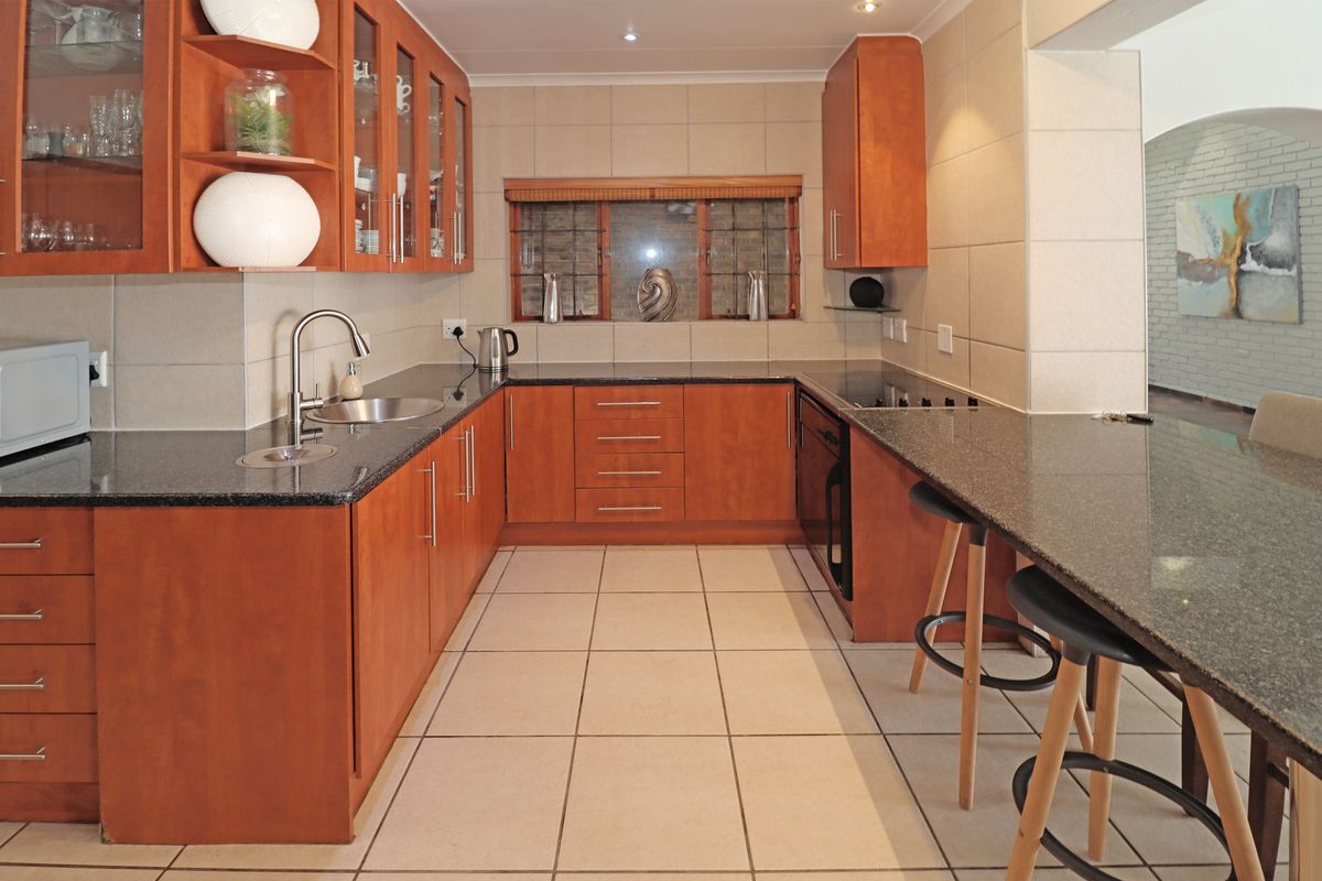A well-maintained kitchen featuring warm wooden cabinetry, granite countertops, a breakfast bar, and neutral ceramic tile flooring.