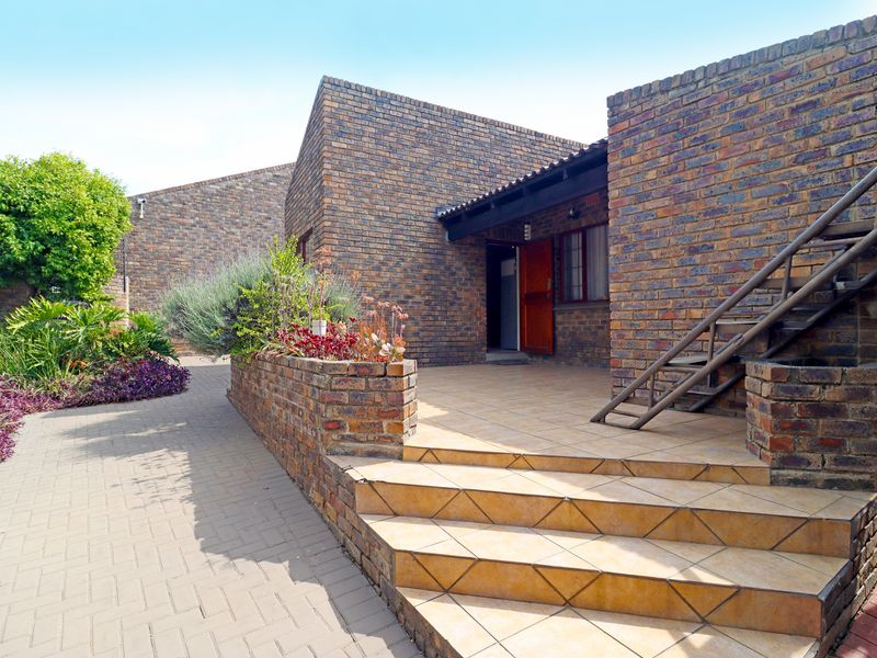 A rear exterior view featuring a face brick facade, a tiled patio area with steps, and a paved walkway leading to the entrance.