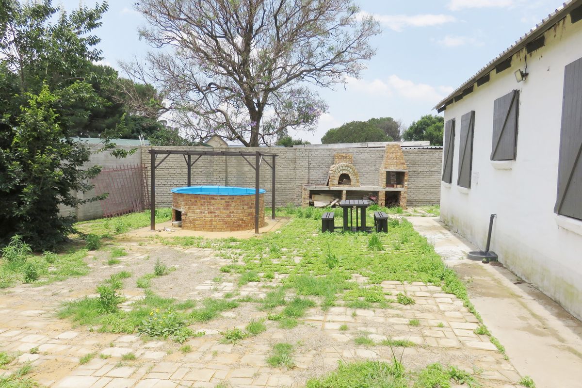 Rear garden area featuring a paved patio, built-in braai, pizza oven, and a raised circular pool, requiring maintenance and landscaping.