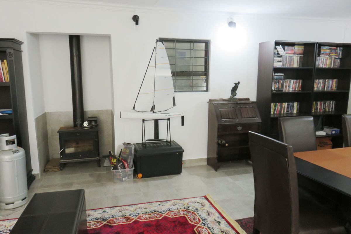 A living area featuring tiled flooring, a freestanding fireplace, and security bars on the window, providing a functional and comfortable space.