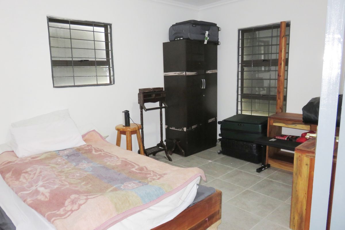 A functional bedroom featuring tiled flooring and windows fitted with security bars, providing a basic and practical living space.