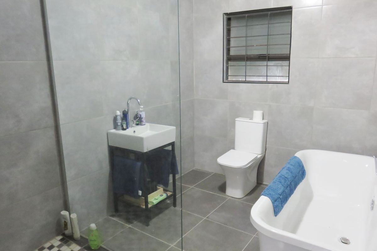 Modern bathroom featuring a freestanding bathtub, glass shower enclosure, wall-mounted basin, and neutral grey floor-to-ceiling tiling.