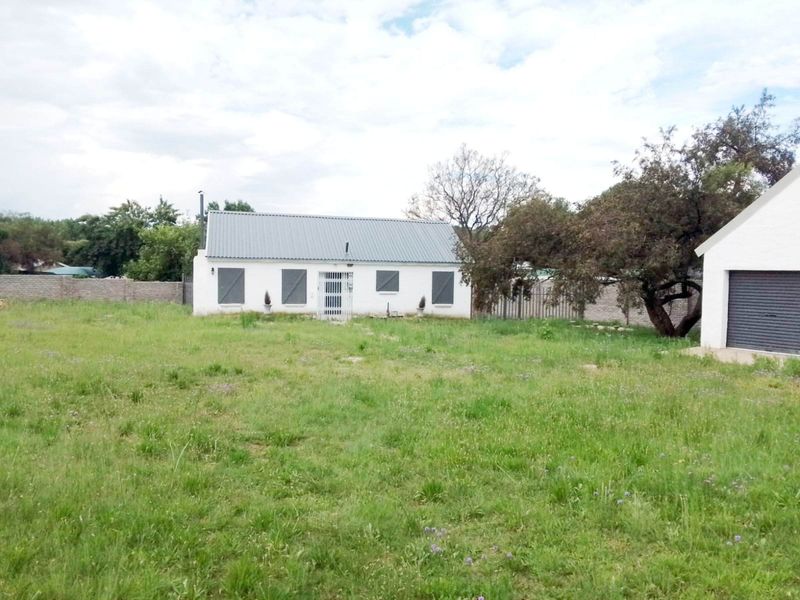 Rear view of the property featuring a single-story dwelling with a metal roof, security shutters, and a detached garage set on a large grassed plot.