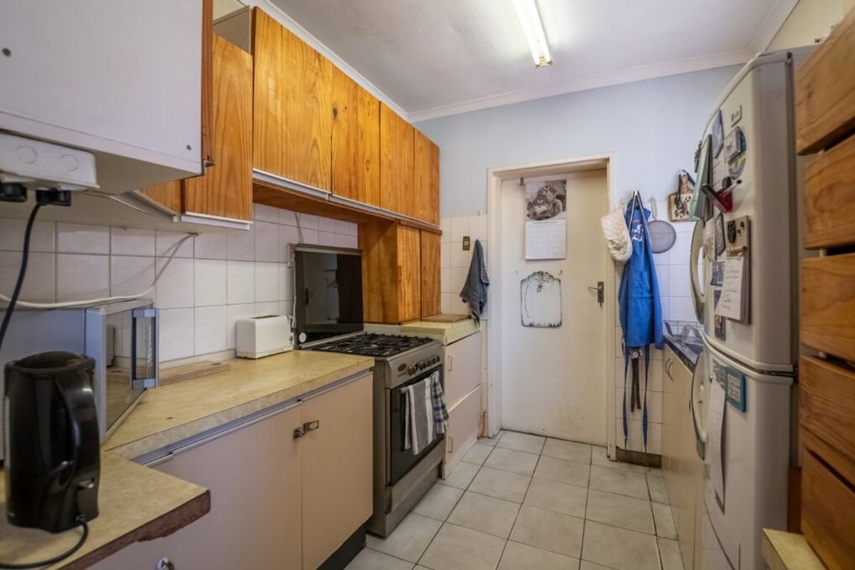 A functional kitchen featuring wooden cabinetry, tiled splashbacks, and a gas stove, offering a dated aesthetic with potential for modern renovation.