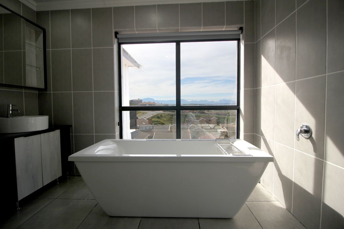 Modern bathroom featuring a sleek freestanding bathtub, vessel sink vanity, and large window with scenic views, finished with contemporary wall and floor tiling.