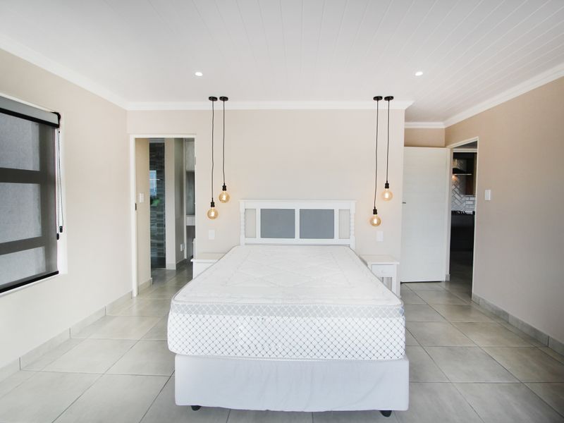 A bright and spacious bedroom featuring neutral wall tones, tiled flooring, a tongue and groove ceiling, and modern pendant lighting.