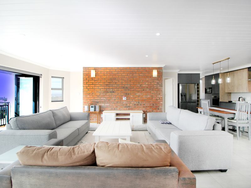 Spacious open-plan living and kitchen area featuring an exposed brick feature wall, modern cabinetry, and large sliding doors leading to an outdoor balcony.