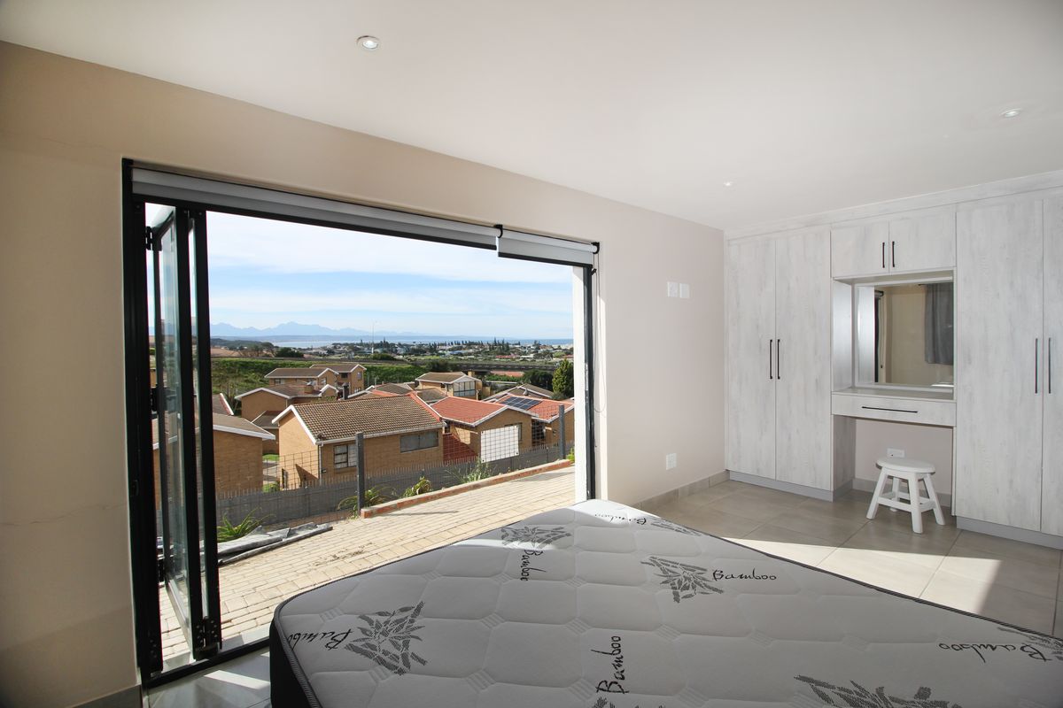 Spacious bedroom featuring built-in cupboards, a vanity area, tiled flooring, and large bi-fold doors opening to a scenic outdoor view.