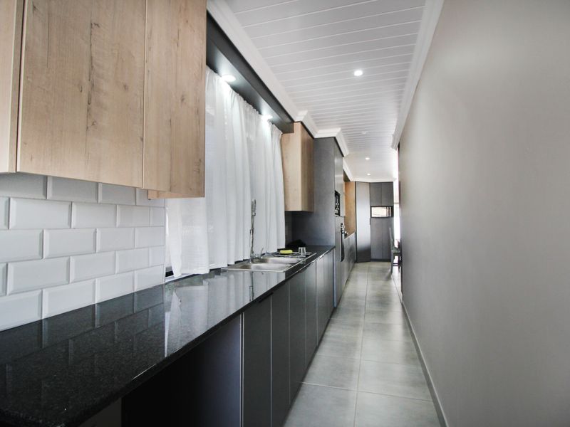 Modern galley-style kitchen featuring sleek dark cabinetry, contrasting light wood upper cabinets, granite countertops, and a classic subway tile backsplash.
