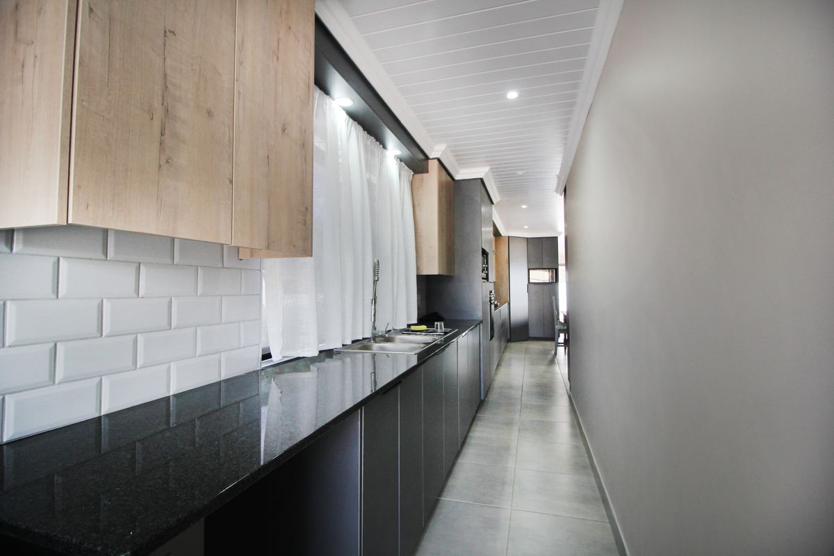 Modern galley-style kitchen featuring sleek dark cabinetry, contrasting light wood upper cabinets, granite countertops, and a classic subway tile backsplash.