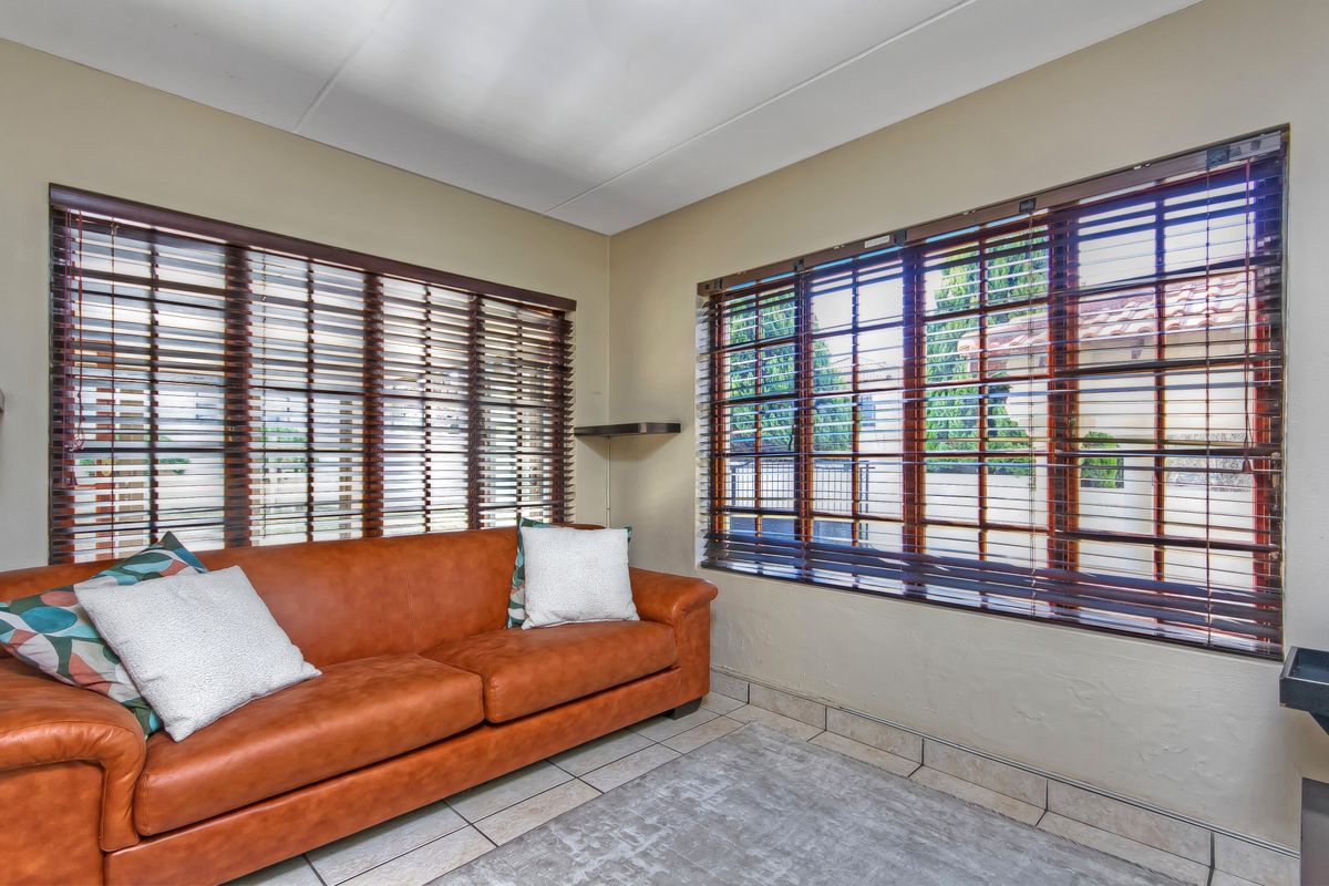 A bright living room featuring tiled flooring and large windows fitted with wooden venetian blinds.