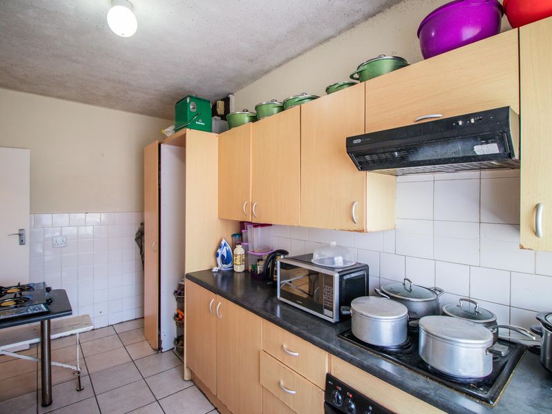 A functional kitchen featuring laminate cabinetry, tiled backsplash, and tiled flooring, equipped with a built-in hob and extractor fan.