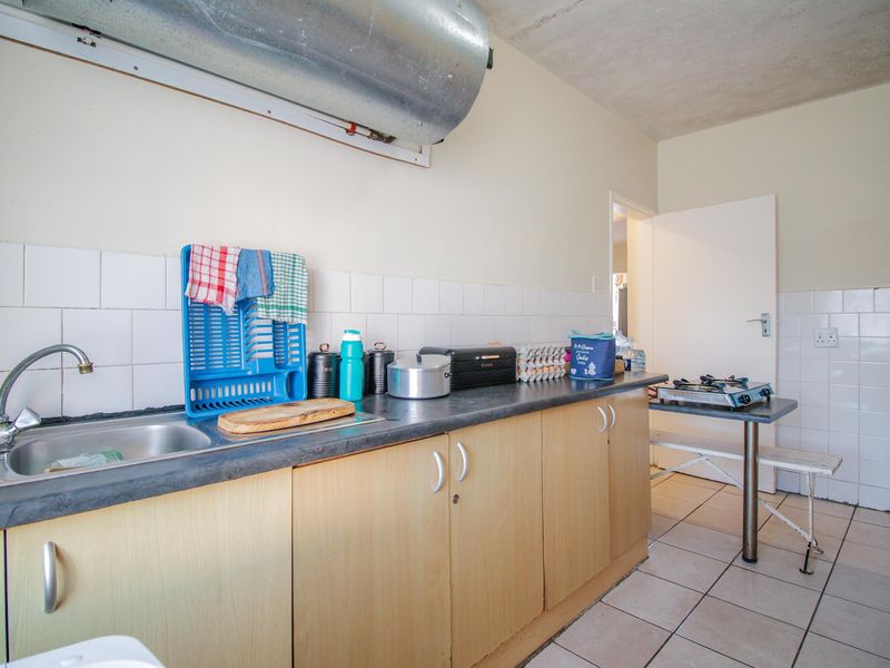 A functional kitchen area featuring laminate countertops, tiled backsplash, and exposed utility infrastructure, offering potential for modernization and aesthetic improvement.