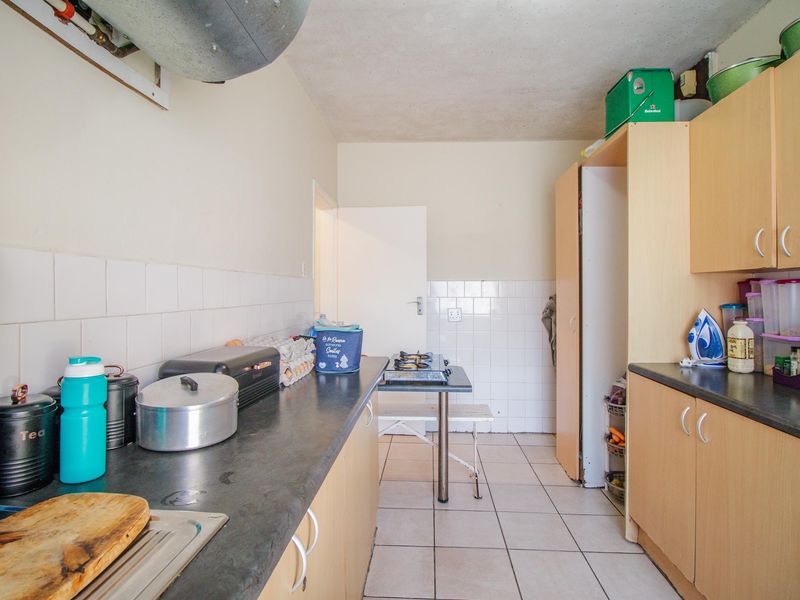 A functional kitchen featuring laminate cabinetry, tiled backsplash, and tiled flooring, offering a practical layout with potential for cosmetic updates.