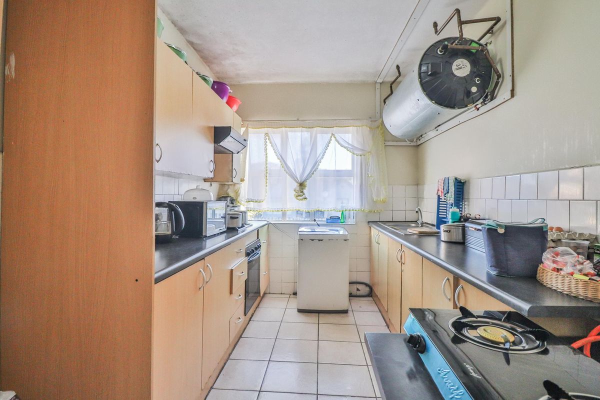 A functional galley-style kitchen featuring built-in cabinetry, tiled surfaces, and an integrated oven, with an exposed geyser unit mounted on the wall.