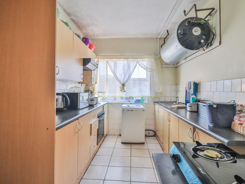 A functional galley-style kitchen featuring built-in cabinetry, tiled surfaces, and an integrated oven, with an exposed geyser unit mounted on the wall.
