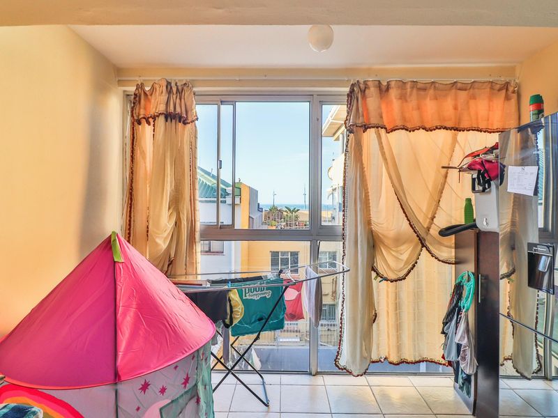 A bedroom featuring tiled flooring and a large sliding window that provides natural light and an urban view.