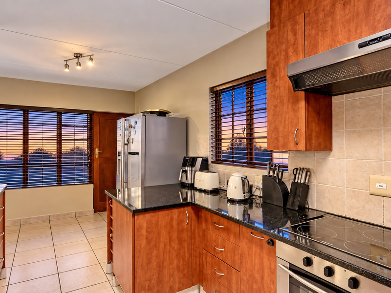 A functional kitchen featuring cherry wood cabinetry, black granite countertops, tiled flooring, and built-in appliances with a view through large windows.