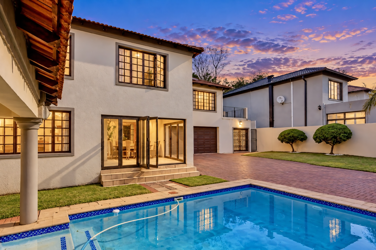 A well-maintained rear exterior view featuring a swimming pool, paved driveway, covered patio area, and bi-fold doors leading into the home.