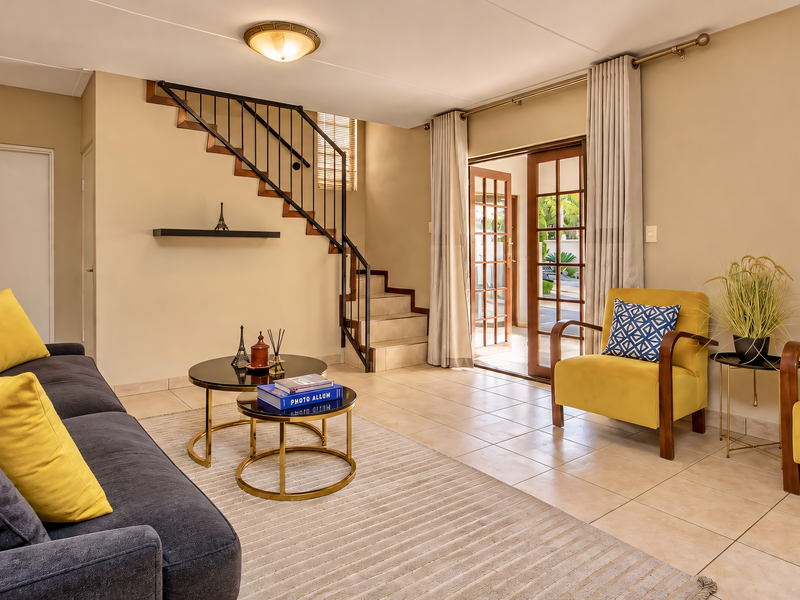 A bright living room featuring tiled flooring, a staircase with a metal railing, and sliding glass doors providing access to the outdoor area.