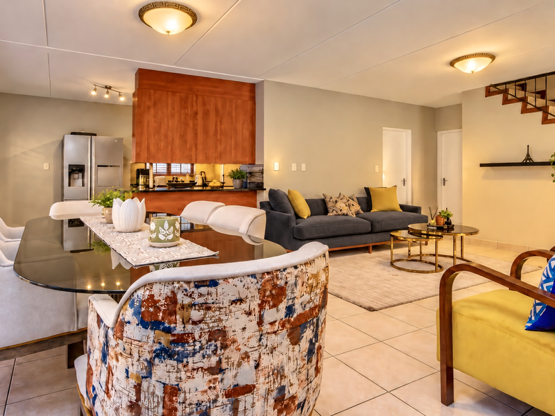 Spacious open-plan living and dining area featuring tiled floors, a modern kitchen with wood-finish cabinetry, and an internal staircase with a metal balustrade.