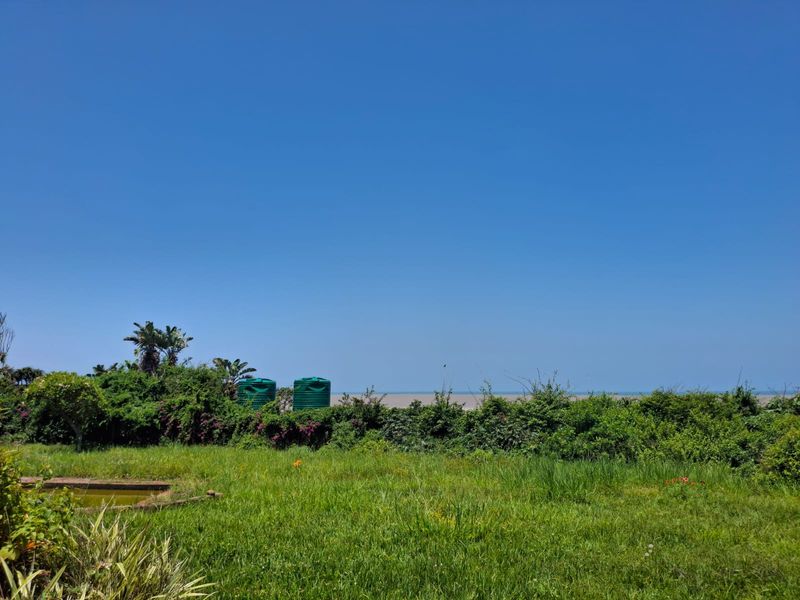 A scenic view overlooking a grassy plot with established vegetation and water storage tanks, offering a clear horizon line.