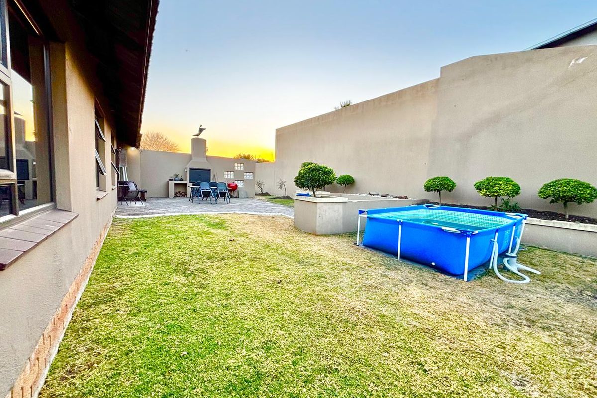 Rear garden featuring a paved patio area with a built-in braai, raised garden beds, and a lawn space.