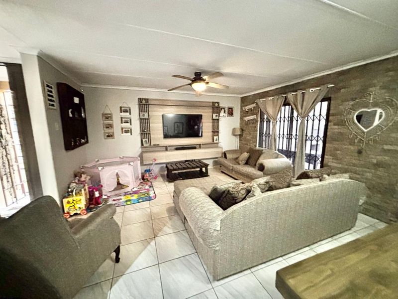Spacious living room featuring a stone accent wall, built-in media cabinetry, tiled flooring, and a ceiling fan, providing a comfortable family living space.