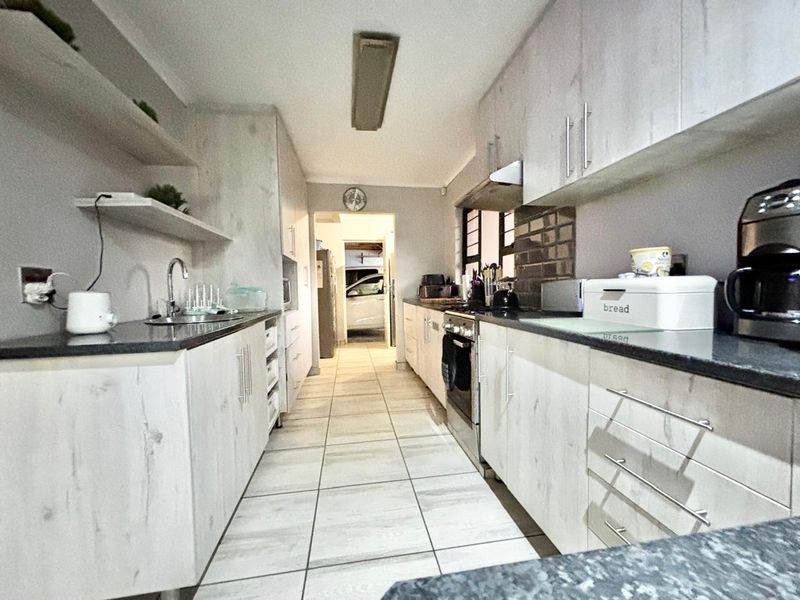 A functional galley-style kitchen featuring light wood-grain cabinetry, dark stone countertops, tiled flooring, and integrated cooking appliances.