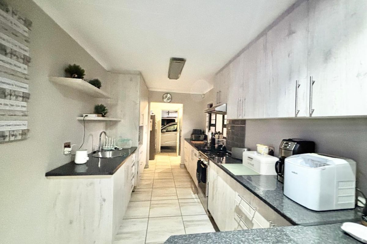A functional galley-style kitchen featuring light wood-grain cabinetry, dark granite countertops, built-in cooking appliances, and tiled flooring with direct access to the garage.