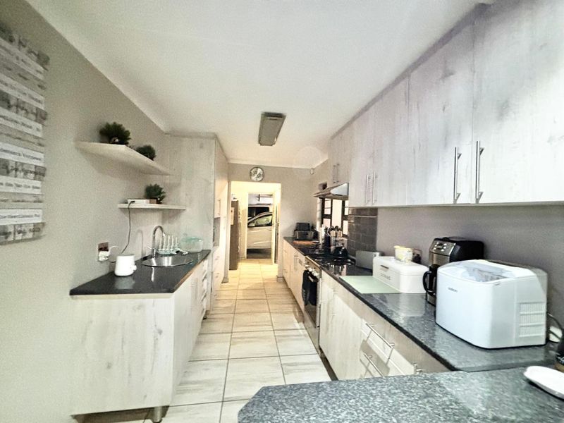 A functional galley-style kitchen featuring light wood-grain cabinetry, dark granite countertops, built-in cooking appliances, and tiled flooring with direct access to the garage.