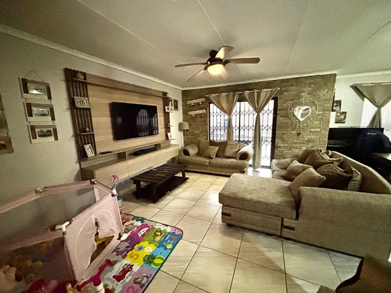Living room featuring a stone accent wall, built-in media cabinetry, tiled flooring, and a ceiling fan.
