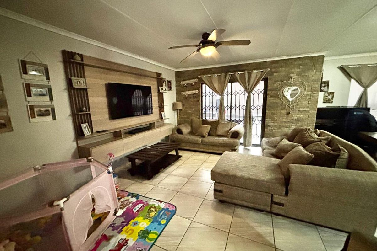 Living room featuring a stone accent wall, built-in media cabinetry, tiled flooring, and a ceiling fan.