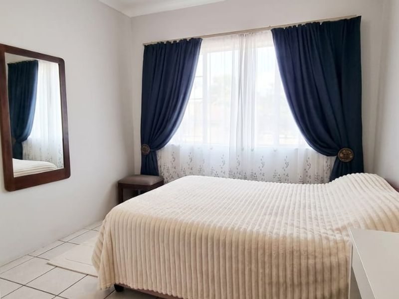 A well-maintained bedroom featuring neutral tiled flooring and large windows with installed curtain rails, providing a bright and comfortable living space.
