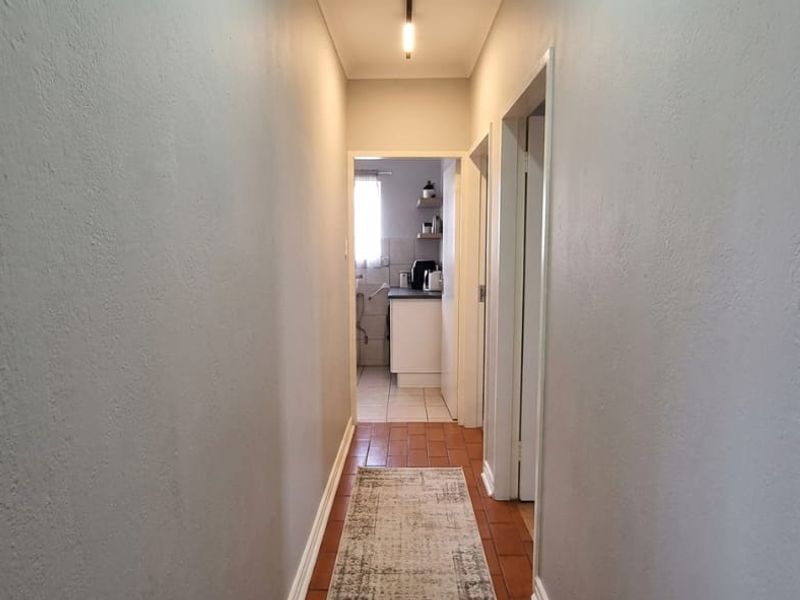 A clean, neutral-toned hallway with tiled flooring, providing access to adjacent rooms including a glimpse of a kitchen area.