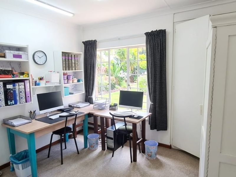 A functional home office featuring built-in shelving, a built-in cupboard, and a window overlooking the garden.