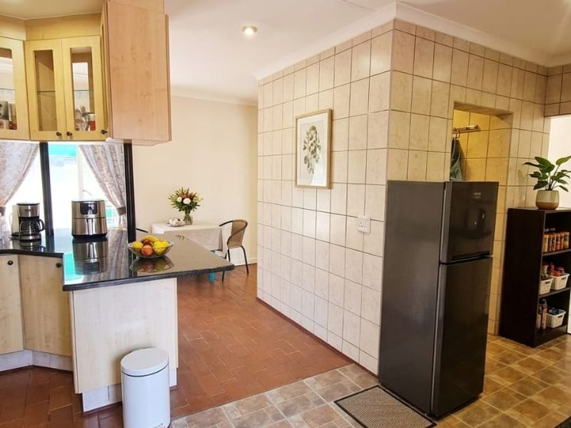 A functional kitchen featuring granite countertops, tiled wall finishes, and ample built-in cabinetry, with an open-plan layout connecting to the dining area.