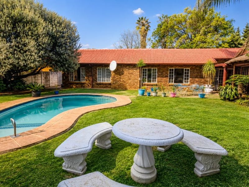 A well-maintained backyard featuring a kidney-shaped swimming pool, lush green lawn, and a brick-clad house exterior with a tiled roof.