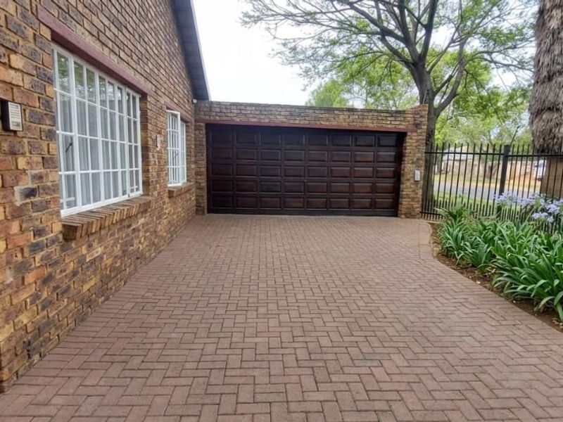 Front exterior view featuring a face brick facade, paved driveway, and a secure garage entrance with steel fencing.