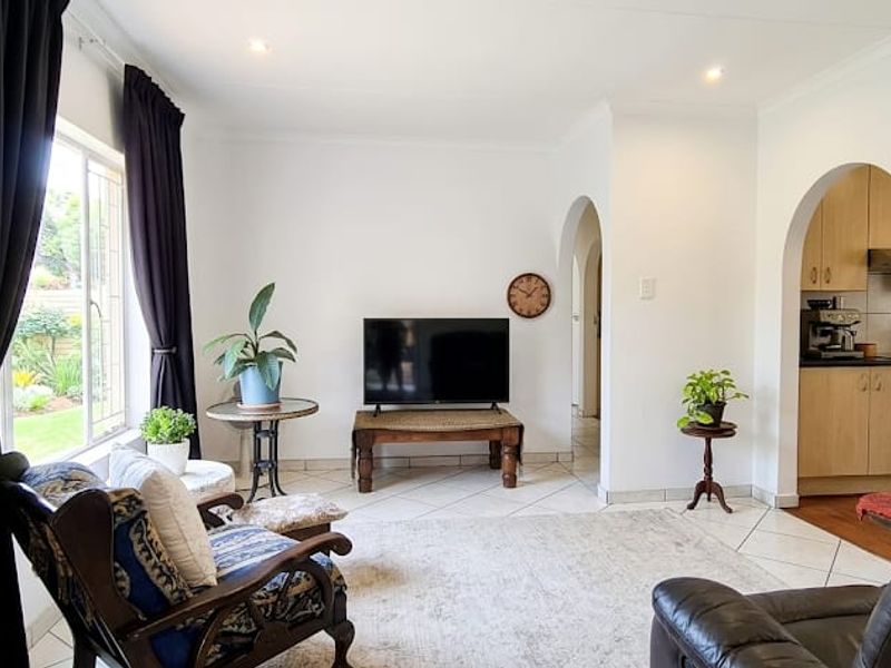 A bright living room featuring tiled floors, recessed lighting, and an arched entryway leading to the kitchen area.