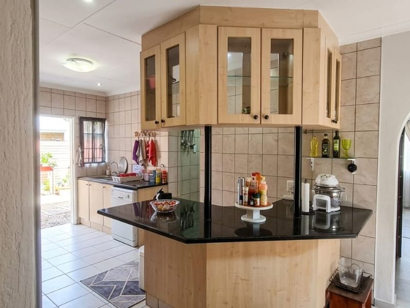 A functional kitchen featuring light wood cabinetry, granite countertops, a tiled backsplash, and a breakfast bar, with an arched entryway leading to adjacent living spaces.