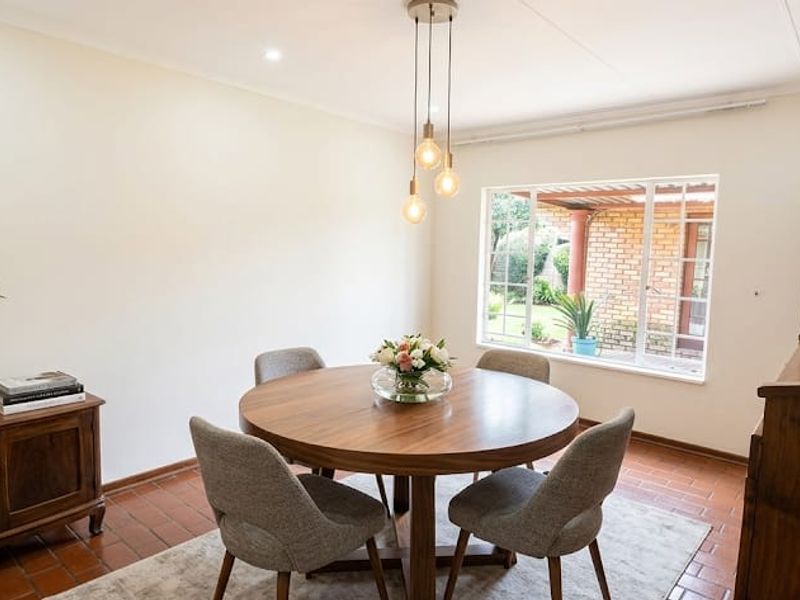 A bright and well-maintained dining room featuring terracotta tile flooring, recessed lighting, and a large window overlooking the garden.