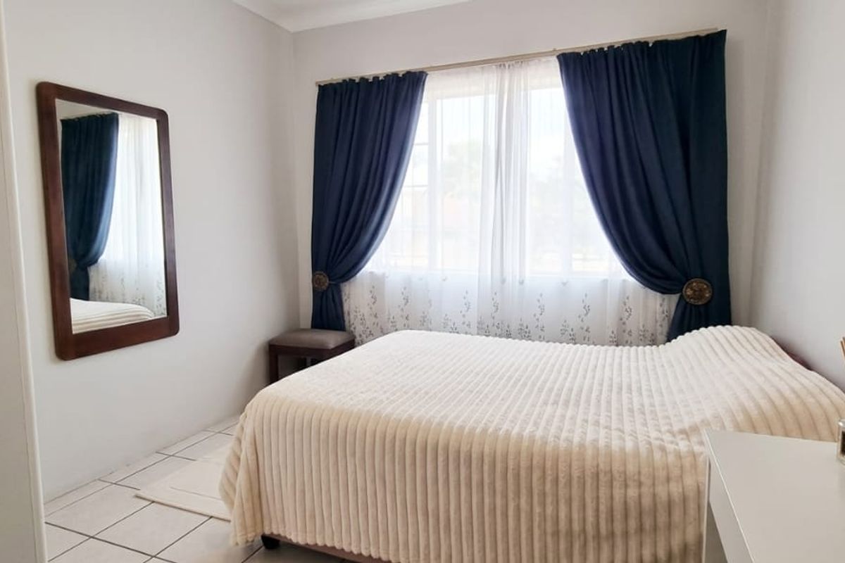 A well-maintained bedroom featuring neutral tiled flooring and large windows with installed curtain rails, providing a bright and comfortable living space.