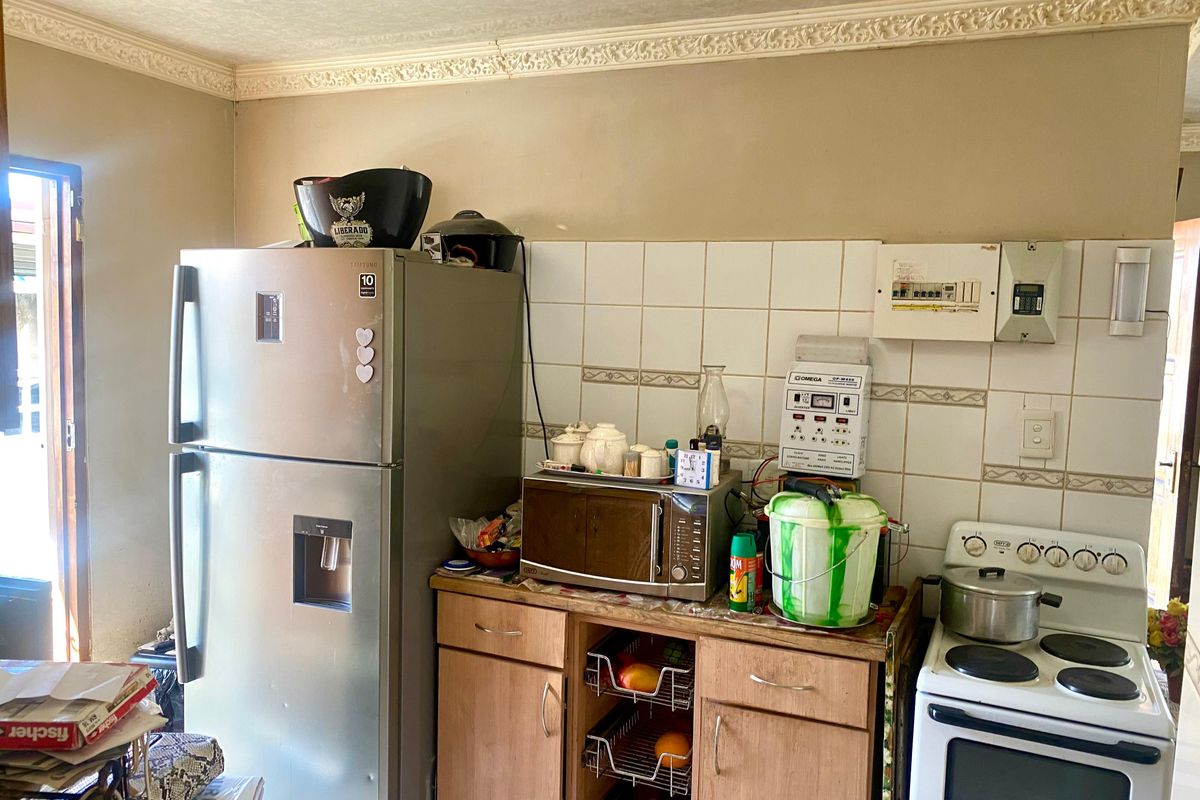 A compact kitchen featuring wooden cabinetry, a tiled backsplash, and an electric stove, with visible wear on the wall finishes and crown molding.