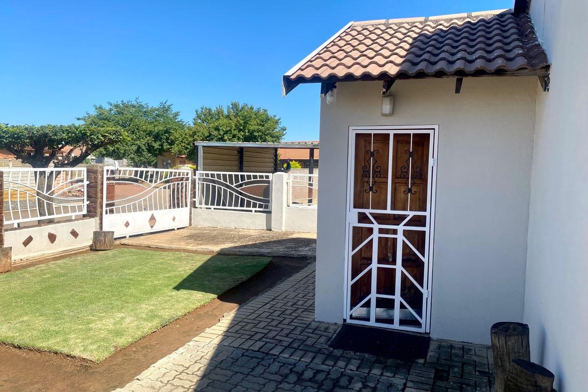 A well-maintained rear exterior view featuring a paved area, a small lawn, and a secure entrance with a metal security gate.