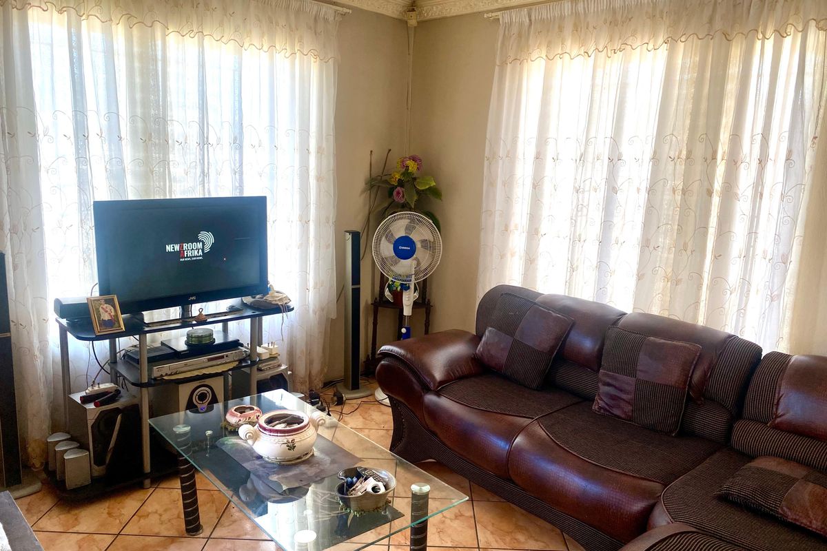 A living room featuring tiled flooring and decorative ceiling cornicing, illuminated by natural light through large windows.